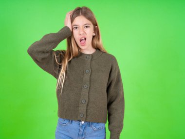 Utanmış, beyaz, yeşil süveter giyen, şok olmuş bir kız, büyük bir şaşkınlık içinde, kapalı mekanda yapboz manken pozları veriyor.