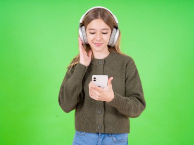 Yeşil kazak giyen mutlu beyaz kız akıllı telefon ekranında odaklanırken kendini iyi hissediyor. İnsanlar, teknoloji, yaşam tarzı