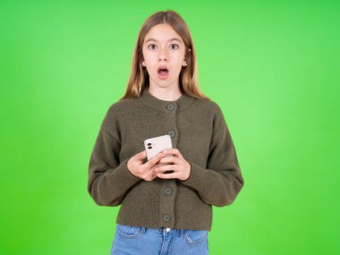 Şok olmuş, beyaz, yeşil kazak giyen güzel bir kız. Ağzını açar. Telefonu tutar, büyük alışveriş reklamları okurdu. 