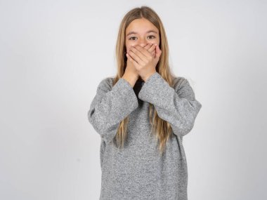 Sersemlemiş, beyaz, gri eşofman giyen güzel bir kız iki elini de ağız üstüne koyar, hayret verici bir şeyden korkar.