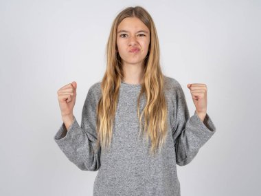 Gri eşofman giyen asabi güzel beyaz kız öfkeyle yanaklarına üflüyor ve yumruklarını kaldırıyor. Öfke ve agresif duyguları ifade ediyor. Öfkeli model
