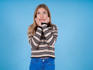 Mavi stüdyo arka planında çizgili süveter giyen üzgün, güzel beyaz bir kızın portresi.