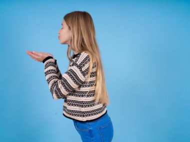 Profil yan görüntüsü, güzel beyaz kız portresi mavi stüdyo arka planında çizgili süveter giyen hava öpücüğü yollayan