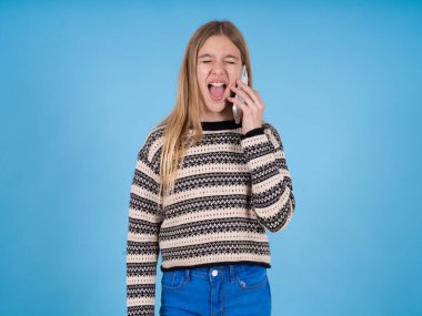 Aşırı duygusal, mutlu, beyaz, çizgili süveter giyen, mavi stüdyo geçmişi olan güzel bir kız telefon görüşmeleri sırasında arkadaşından komik bir hikaye duyuyor.