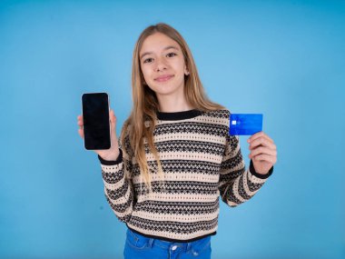 Mavi stüdyo geçmişi üzerine çizgili süveter giyen güzel beyaz bir kız elinde akıllı telefon ve kredi kartı ile banka hesabı açmış, gülümsüyor ve çevrimiçi alışveriş uygulaması tavsiye ediyor.