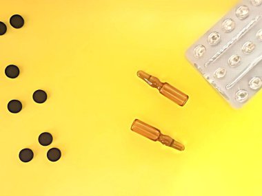 İlaçlar, aktifleştirilmiş karbon ve ampullü siyah haplar sarı arka planda..