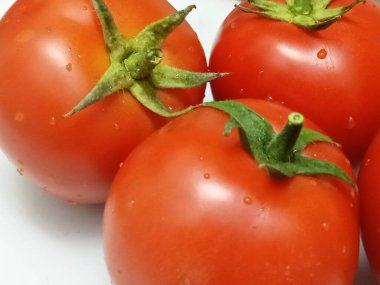 Yeşil saplı birkaç olgun kırmızı domates ve yüzeyinde küçük su damlaları..