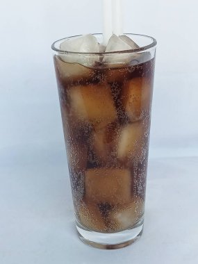 Koyu bir içecek ve buz dolu bir bardak. Bardaktaki parıltıyı ve içecekteki kabarcıkları görebilirsiniz. Bu da karbonatlı ya da köpüklü olduğunu gösterir..