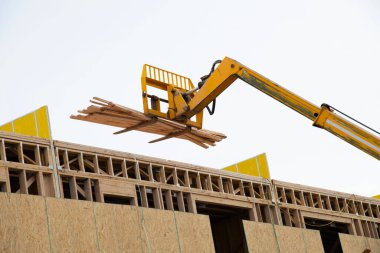 Kontrplak çerçeveli, modern iskan evi ve kereste çerçeveli kiriş apartman kirişi getiren bir forklift.