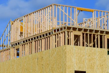 new residential construction house framing against a blue sky plywood plank site window