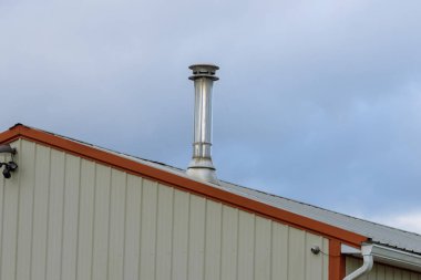 Evin çatısındaki metal baca, mavi gökyüzü arka planındaki yeni parlak baca borusu modern üst hava yükleme