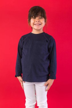 Mavi kazak ve beyaz pantolon giyen, kırmızı arka planda kameraya poz veren gülümseyen siyah saçlı bir kızın portresi. Çağrı merkezi kavramı, ara, konuş ve dinle.