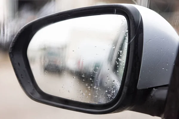 Rearview mirror with raindrops and blurred background, in a gray, cloudy environment. Concept of rain, winter, sadness, dusk, darkness, fear, terror.