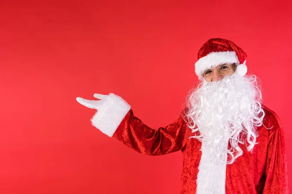 一个穿得像圣诞老人的人 用手指着侧面 背景是红色的 圣诞节 消费主义和幸福概念 — 图库照片