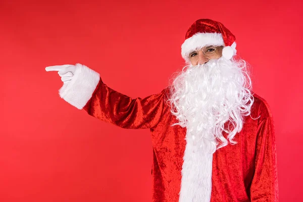 一个穿得像圣诞老人的人 用手指着侧面 背景是红色的 圣诞节 消费主义和幸福概念 — 图库照片
