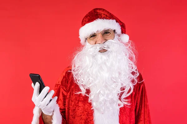穿得像圣诞老人的男人 拿着手机 背景是红色的 圣诞节 消费主义和幸福概念 — 图库照片