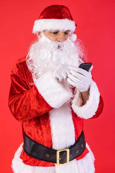 サンタクロースの格好をした男が携帯電話に赤い背景で相談していた クリスマス お祝い 贈り物 消費主義と幸福の概念 — ストック写真