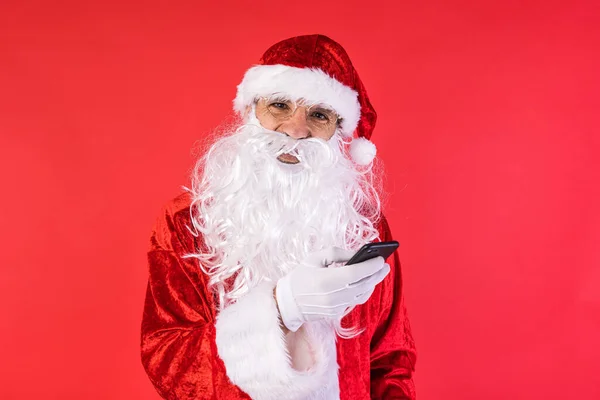 Άντρας Ντυμένος Άγιος Βασίλης Συμβουλεύεται Κινητό Του Τηλέφωνο Κόκκινο Φόντο — Φωτογραφία Αρχείου