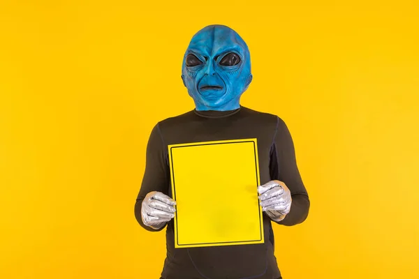 Man with alien mask with a blue head, holding a yellow sign. Concept of bizarre, extraterrestrial, funny, informative, weird and weird.