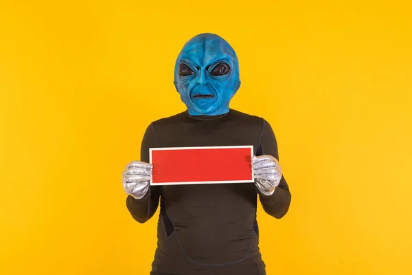Man with alien mask with a blue head, holding a red sign. Concept of bizarre, extraterrestrial, funny, informative, weird and weird.