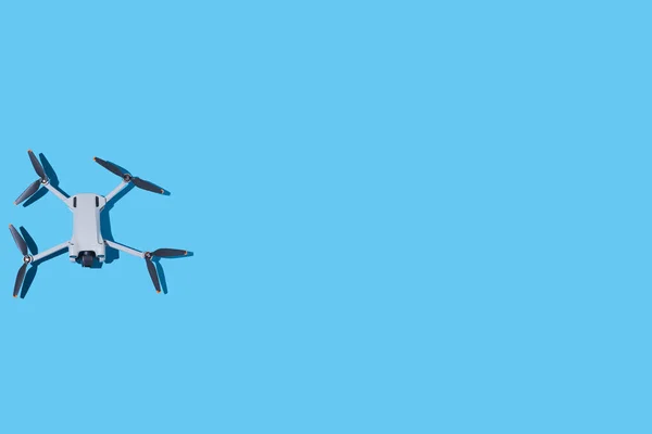 Gray drone, with photo and video camera, and dark propellers, on the left side, on a blue background. UAV, fly, spy, altitude, unmanned, technology and futuristic concept.