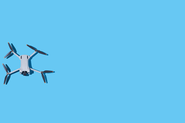 Gray drone, with photo and video camera, and dark propellers, on the left side, on a blue background. UAV, fly, spy, altitude, unmanned, technology and futuristic concept.