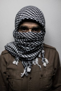 Beyaz arka planda, yüzünü koyu gölgelerle kaplayan, Filistin başörtüsü ya da Shemagh takan bir askerin portresi. Milis, terörizm, savaş, Filistin, İsrail, korku, çatışma kavramı.