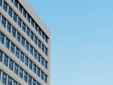 Cam pencereli modern bina köşesi ve berrak mavi gökyüzü arkaplanı.