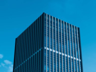 Uzun minimalist cam kule berrak mavi gökyüzünü yansıtıyor.