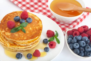 Beyaz tabakta servis edilen taze yaban mersinli, ahududulu ve ballı Amerikan gözlemeleri. Sağlıklı sabah kahvaltısı.