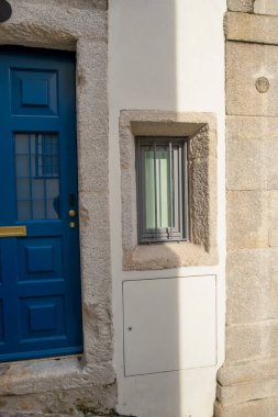 Küçük bir pencerenin portresi ve güneş ışığında mavi bir kapı