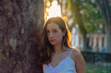 Bir ağacın yanında kameraya bakan güzel bir kadının yatay yakın çekimi.