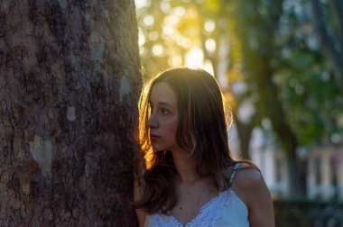 Bir ağacın yanında duran genç ve güzel bir kadının yatay yakın çekimi.