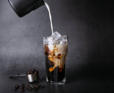 Pour milk make latte coffee into a transparent glass with ice. and roasted coffee beans on a black background studio photo