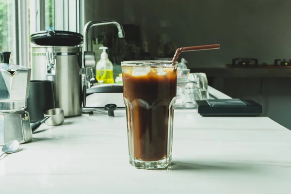 Iced black coffee on the glass on a marble bar with equipment to brew beverages make coffee at home