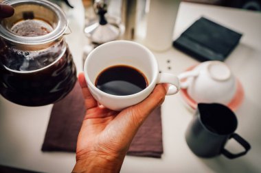 Close up hand pouring coffee drip in a jug into the white cup with equipment, tool brewing with equipment at kitchen home at white kitchen home