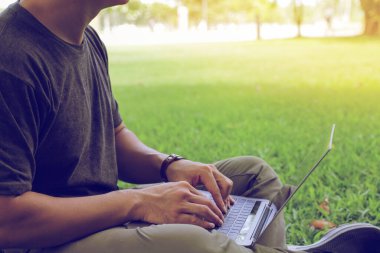 Asian young man 30s looking stock tickers or graphs cryptocurrency trading platforms on the laptop working outside