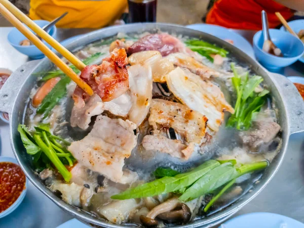 木製の箸でグリルポークを手に 熱い鍋でタイのバーベキュー レストランで食べる熱いストーブの休日の家族のグリルポーク スマートフォンの写真 — ストック写真
