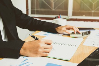 businessman hand using calculator Calculating bonus(Or other compensation) to employees to increase productivity. Writing report paper on the desk working from a home office. Selective Focus