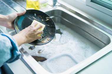 Close-up of a woman washing dishes with dirty food scraps Clean in the sink until the kitchen counter at home.