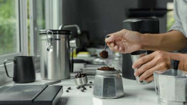 Paslanmaz kaşık üzerinde toz kahve. İnsanlar espresso için kavrulmuş kahve koyuyorlar. İçinde İtalyan Moka demliği, kahve hazırlayan ekipman gereçleri var.