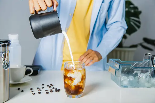 Barista pouring milk,iced latte coffee into a transparent glass with ice. and roasted coffee beans on a black background studio photo