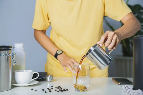 person using pitcher Pour brewed coffee and brew cold black coffee on a mug with roasted Arabica beans on a white table and coffee maker. home made coffee