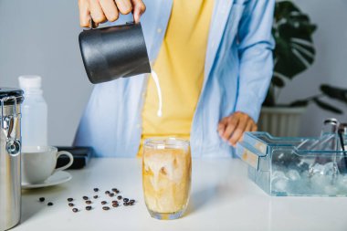 Barista bardağa süt dolduruyor, masaya buzlu kahve hazırlıyor..