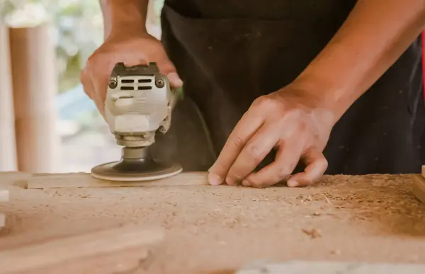 carpenter is sanding wood using an electric wood sander to smooth the wood surface on a workbench at his factory. Small Business , working as your own boss at home Concept