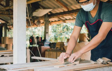 Asyalı marangoz fabrikasında bir masa masasının üzerine bir kutu yapmak için dairesel testere kullanıyor. Ev konseptinde kendi patronun olarak çalışıyorsun.