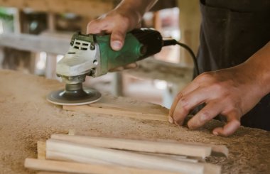 Asyalı marangoz fabrikasındaki tezgahın ahşap yüzeyini pürüzsüz hale getirmek için elektrikli odun zımpara makinesi kullanıyor. Küçük işletme, evde kendi patronun olarak çalışmak.