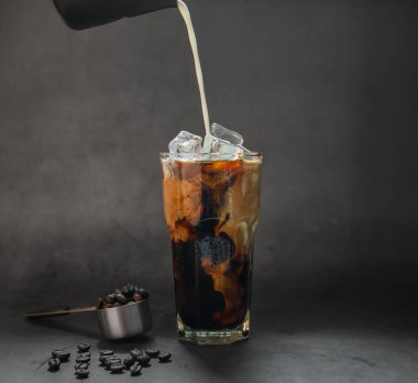 Süt, buzlu şeffaf bardağa kahve yapar. Ve siyah arkaplan fotoğrafında kahve çekirdekleri kavurması.