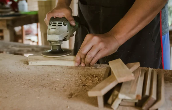Asian carpenter is sanding wood using an electric wood sander to smooth the wood surface on a workbench at his factory. Small Business , working as your own boss at home Concept