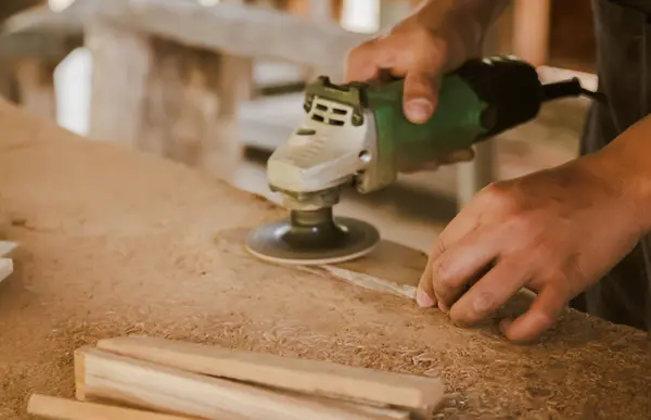 Asian carpenter is sanding wood using an electric wood sander to smooth the wood surface on a workbench at his factory. Small Business , working as your own boss at home Concept